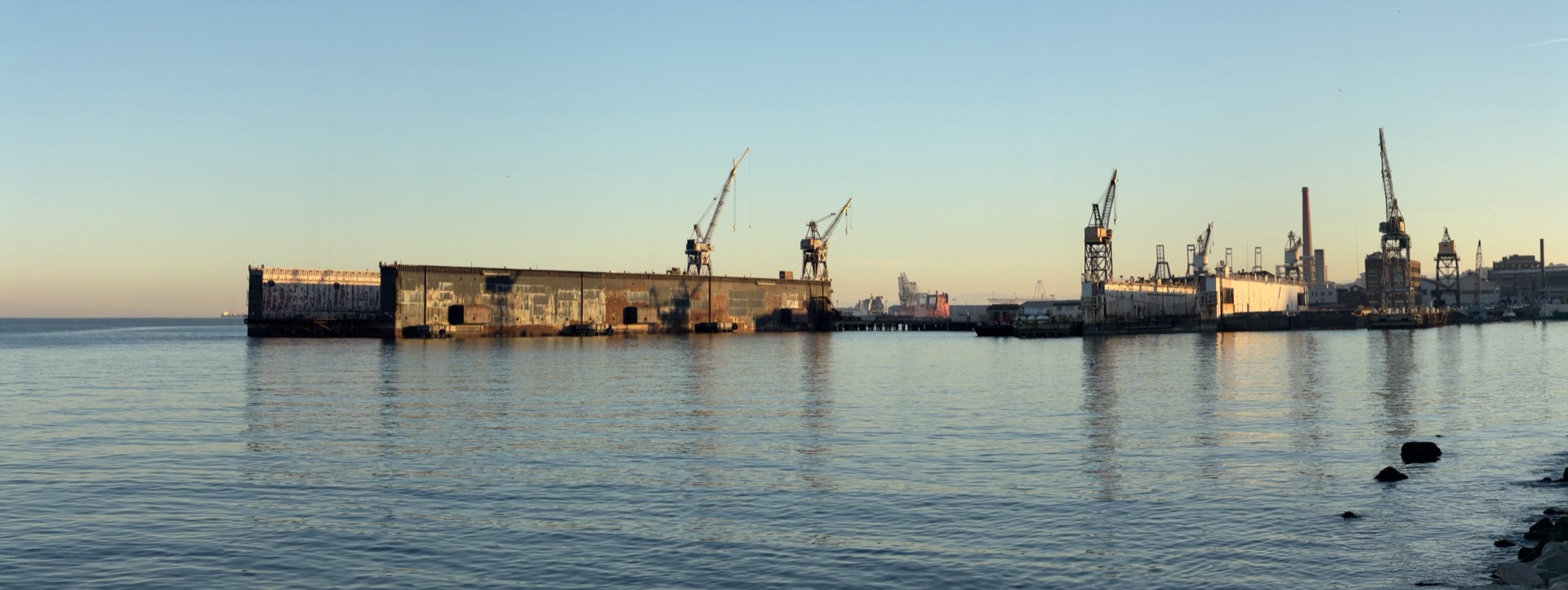 A floating dry dock and cranes on the San Francisco waterfront at sunset