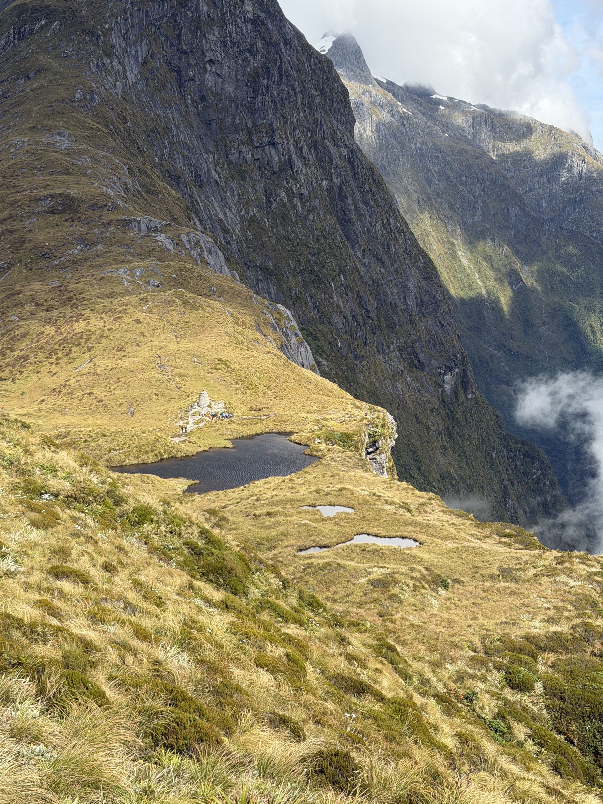 Tarns and the memorial cairn at Mackinnon Pass, below a granite wall