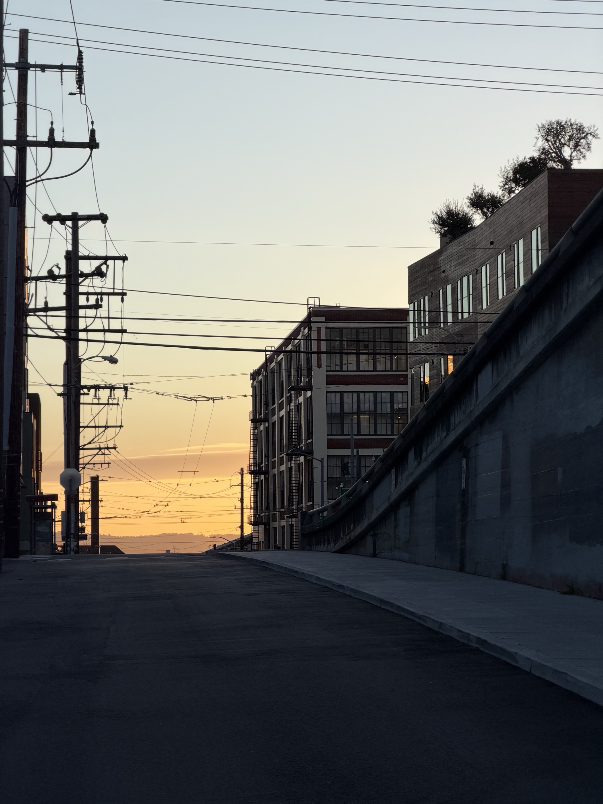 Sunrise down a street of power lines and brick industrial buildings