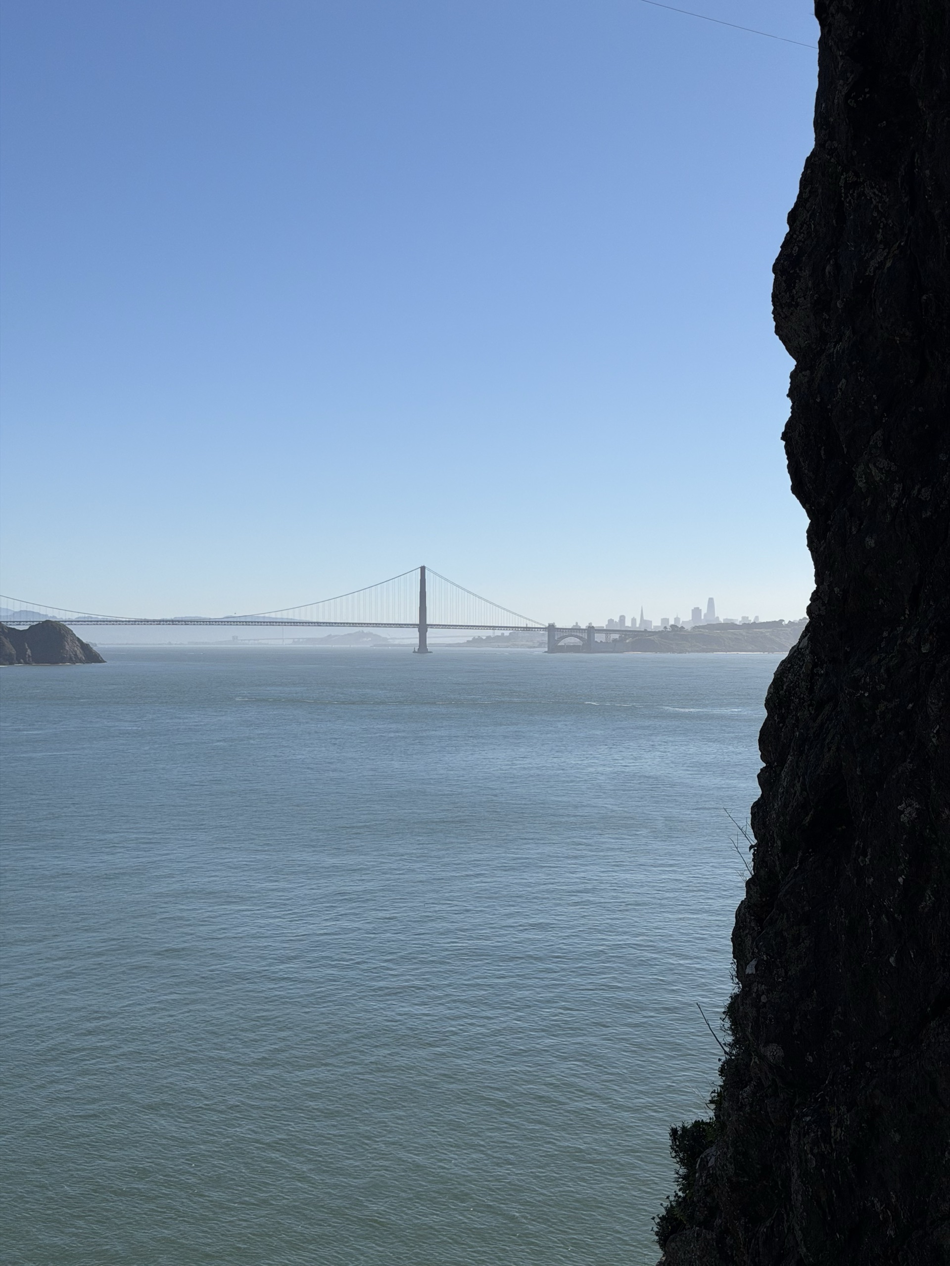 The Golden Gate Bridge and San Francisco skyline past a dark cliff