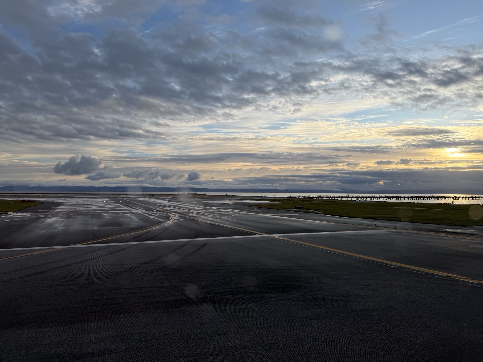 Wet airport tarmac under a cloudy sunrise beside the bay