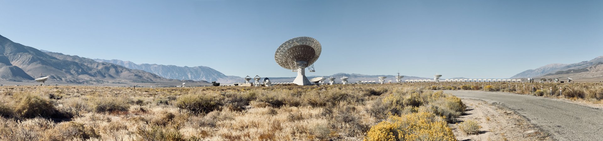 Panorama of a large radio dish and a line of smaller dishes across the sagebrush of the Owens Valley