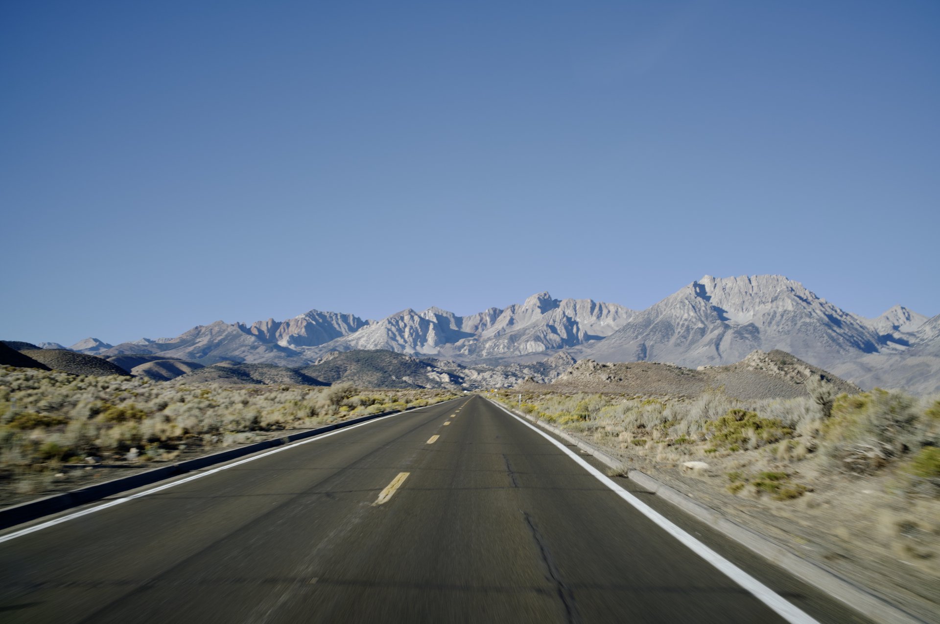 An empty two-lane highway running through sagebrush toward the Sierra crest