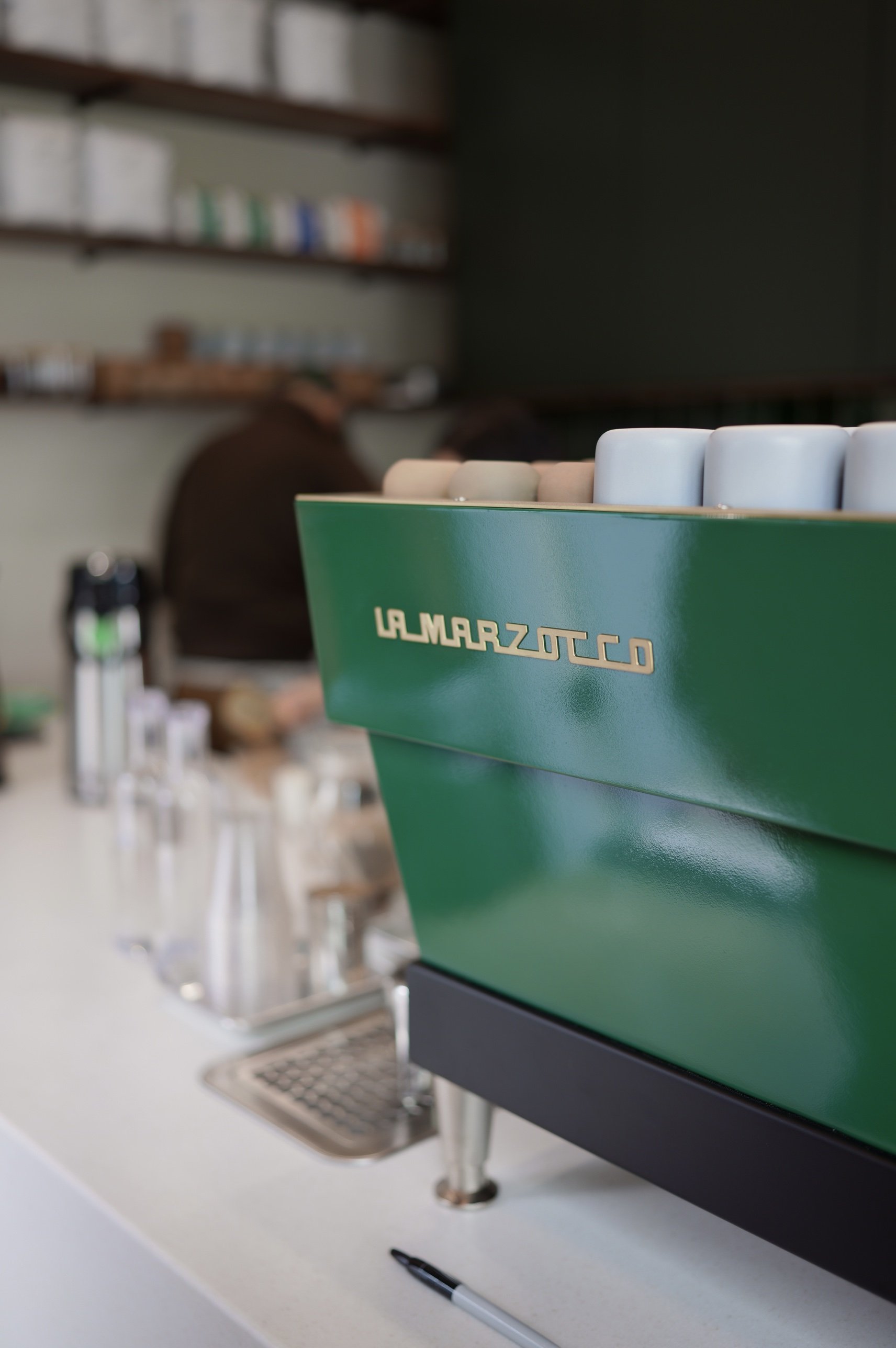 A green La Marzocco espresso machine at Chula Café, with cups stacked on top